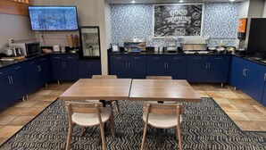 A modern kitchen with dark blue cabinets, a wooden table, and a patterned rug. - AmericInn by Wyndham Stillwater (Stillwater)