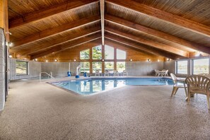 Una piscina interior con techo de madera alto, paredes de azulejos y vistas a árboles fuera.