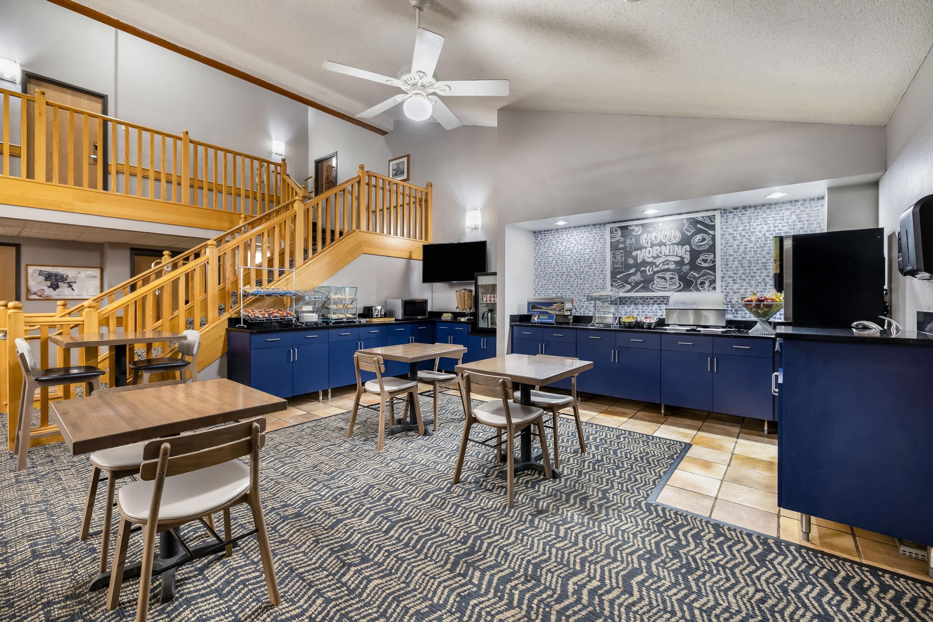 Une cuisine spacieuse avec un escalier en bois, un coin repas avec une table et des chaises, et un îlot de cuisine équipé d’un réfrigérateur.