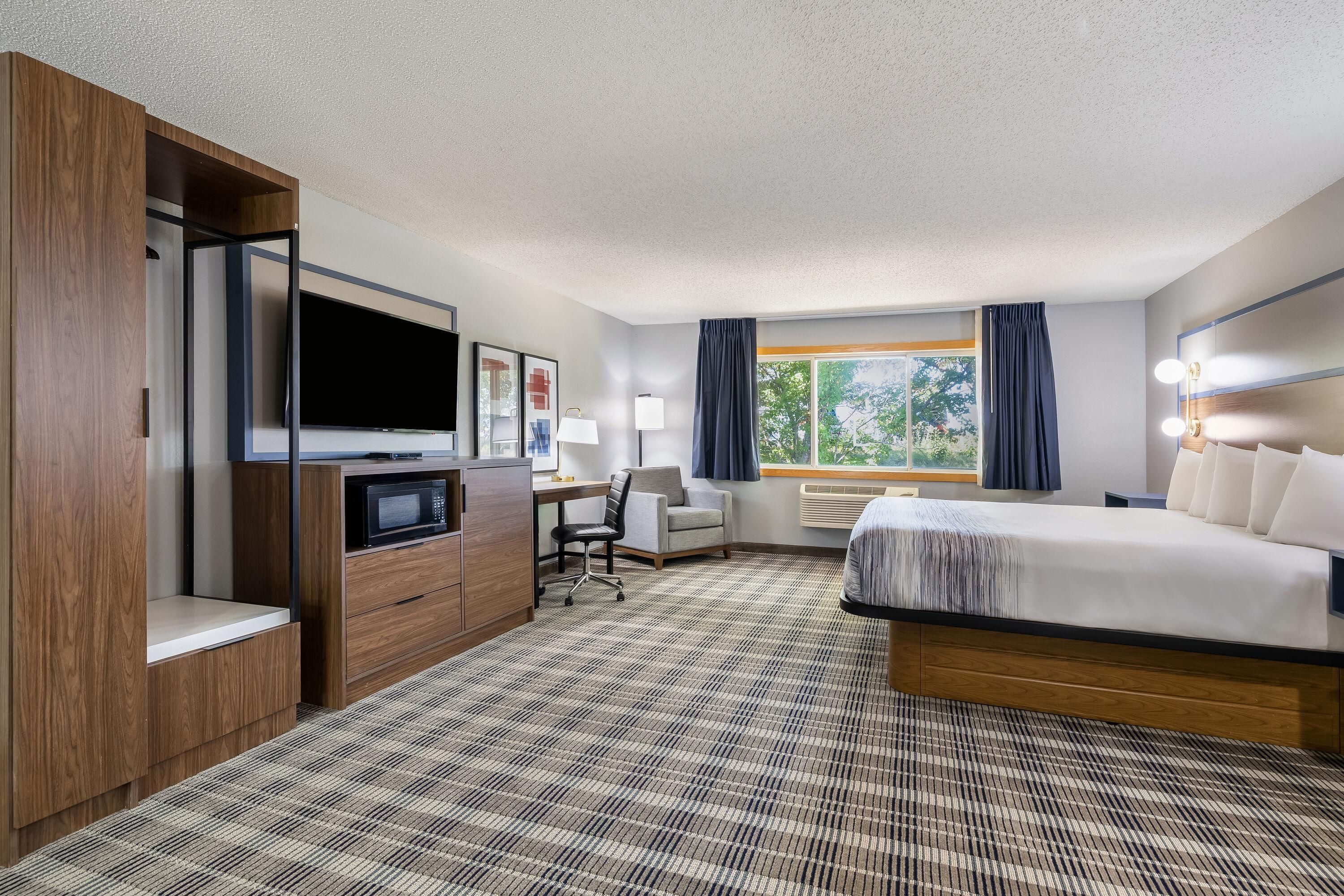 A hotel room with a bed, desk, chair, television, and a large window with curtains.