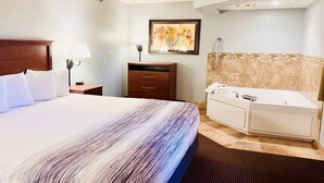 A hotel room with a large bed, a bedside table with a lamp, a dresser, a bathroom with a bathtub, and a framed floral artwork on the wall. - AmericInn by Wyndham Stillwater (Stillwater)