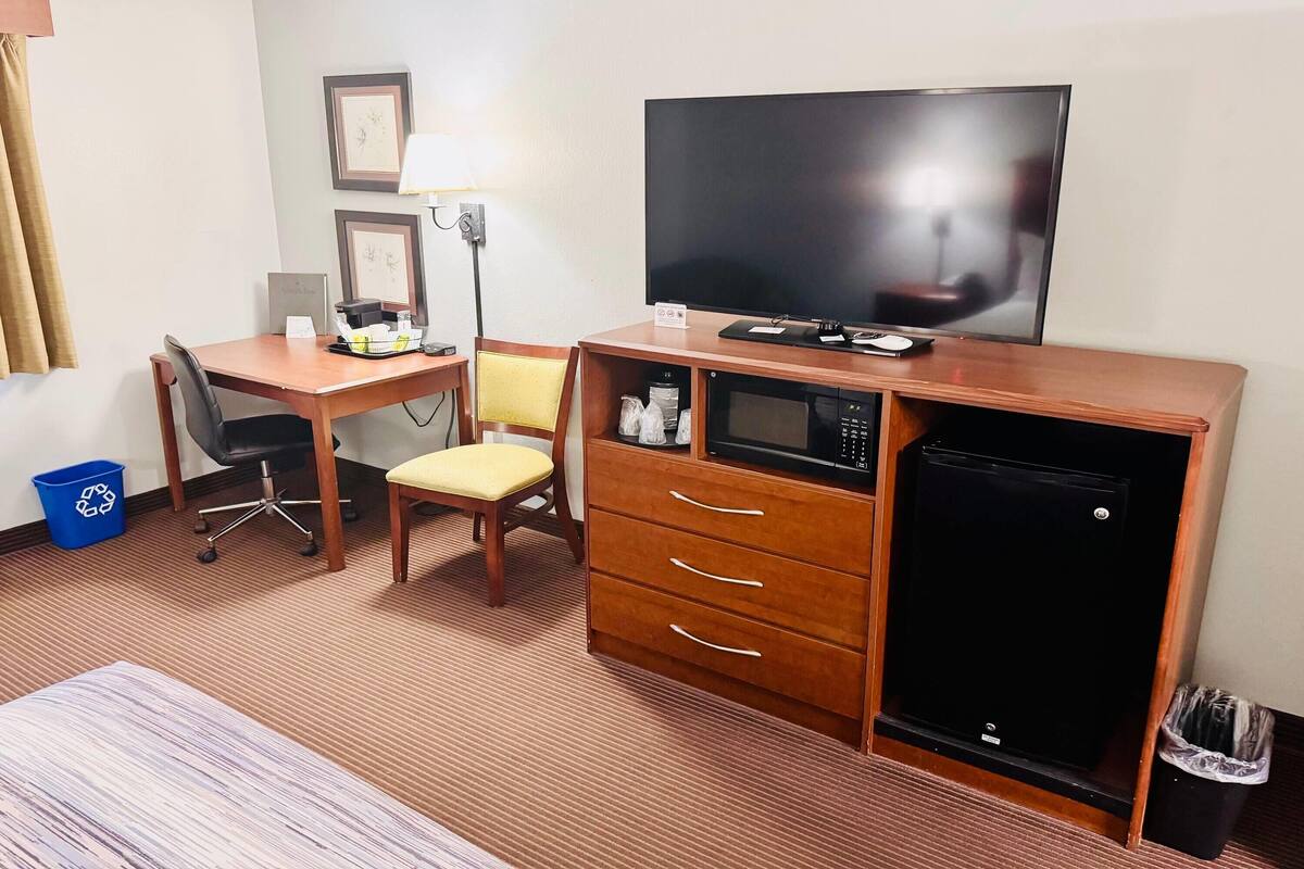 Een hotelkamer met een houten bureau, een stoel, een televisie, een magnetron en een koelkast.
