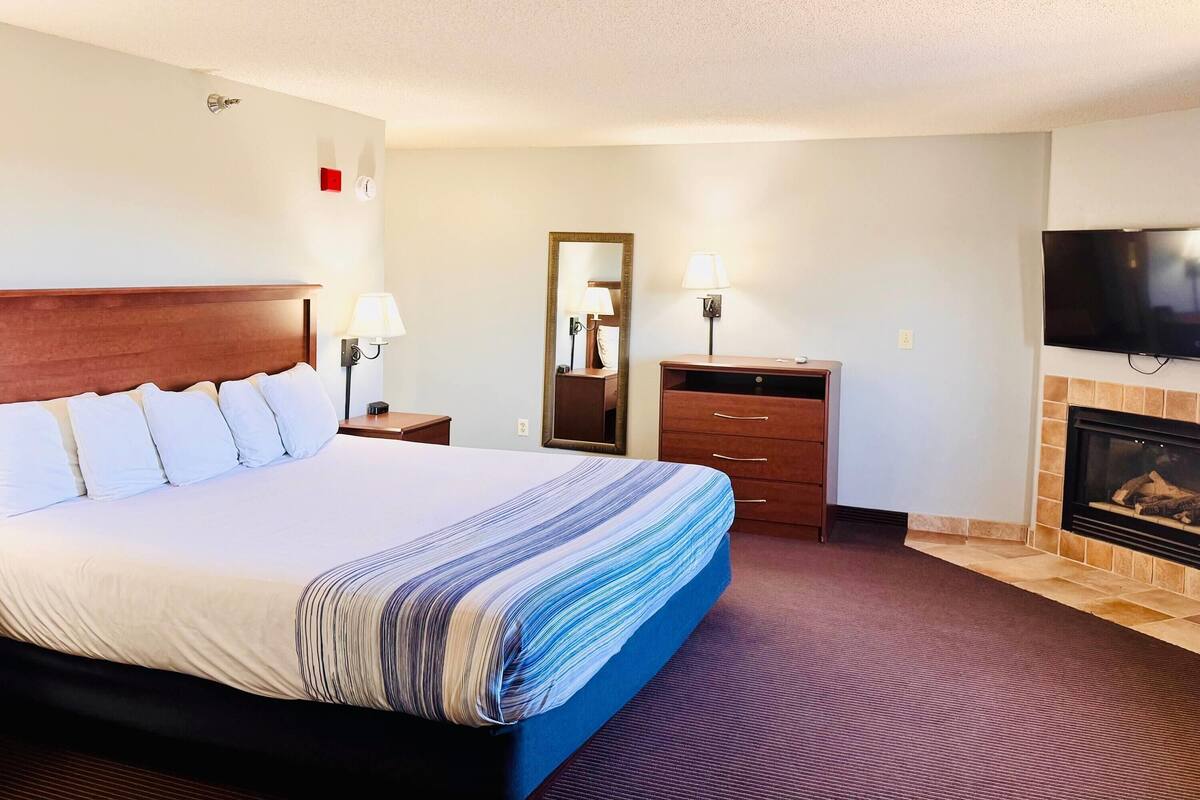 Een hotelkamer met een groot bed, een televisie, een open haard en een spiegel.
