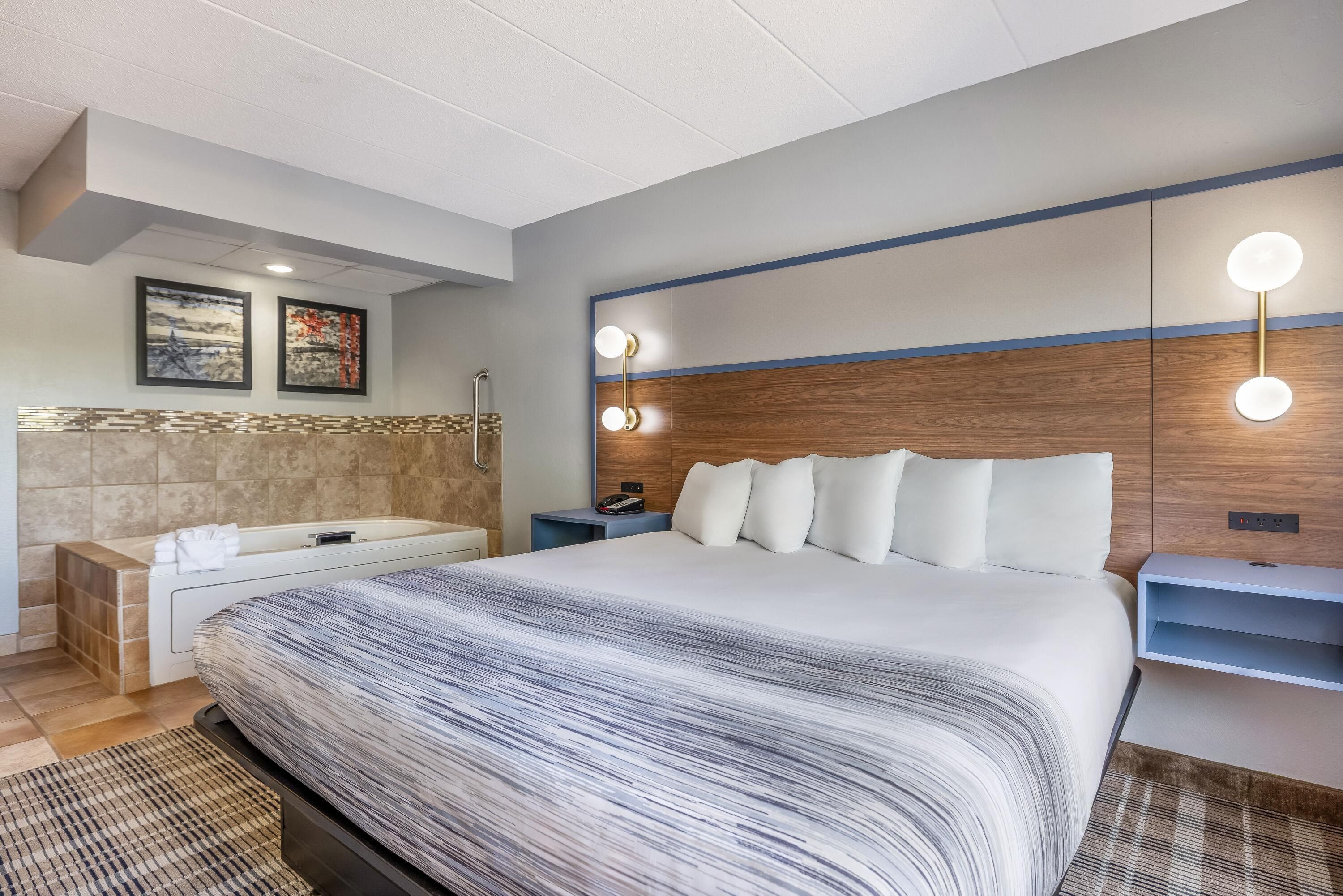 Habitación de hotel moderna con una cama grande, una bañera empotrada, un tocador con espejo y una lámpara de pared.