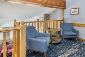 A room with a wooden staircase, two blue armchairs, a small round table, and a stone wall.