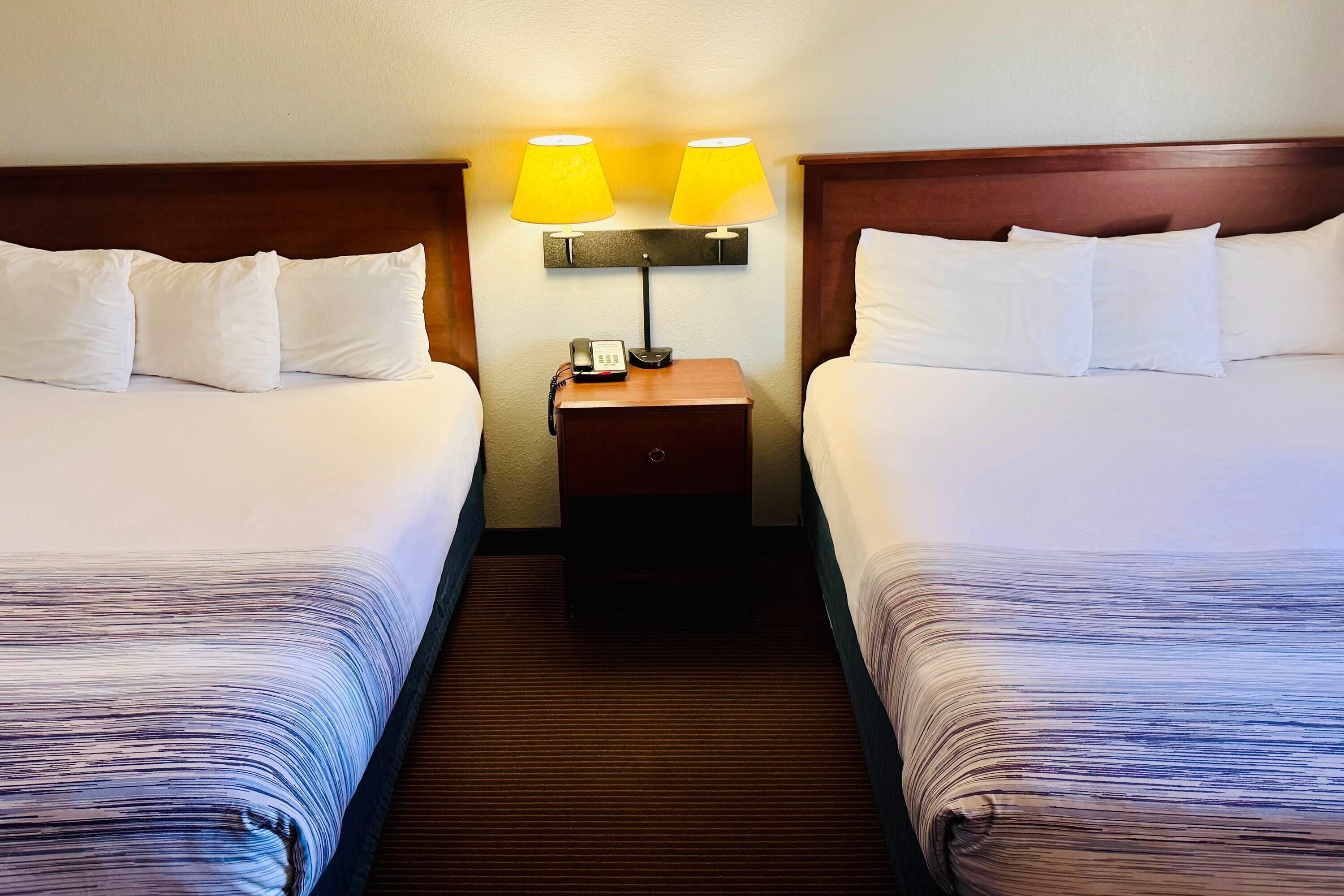 A hotel room with two beds, a nightstand with a lamp, and a telephone.