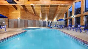 A swimming pool with blue tiles, wooden beams, and blue lounge chairs.