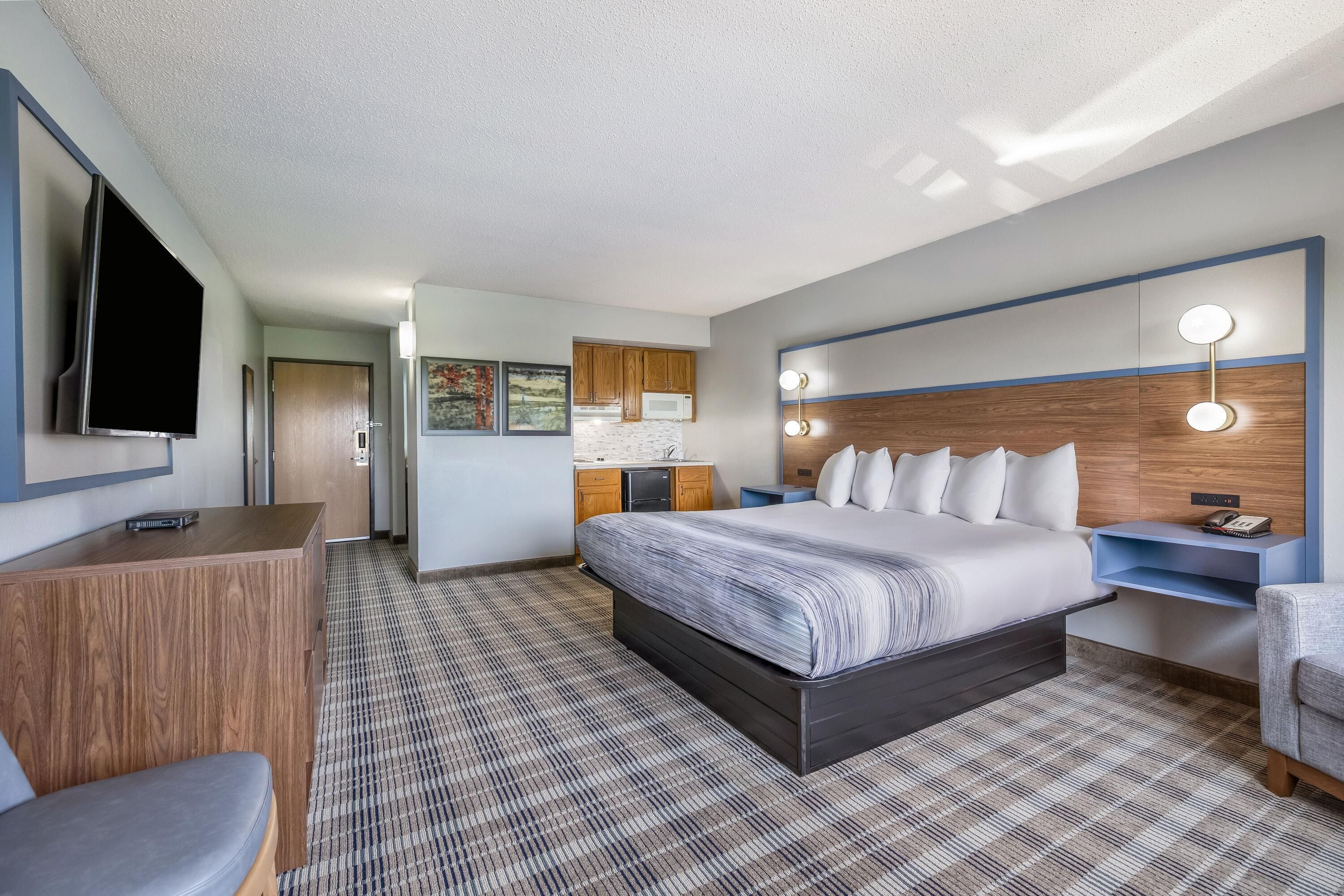 A hotel room with a bed, bedside table, TV, and a desk with a chair.