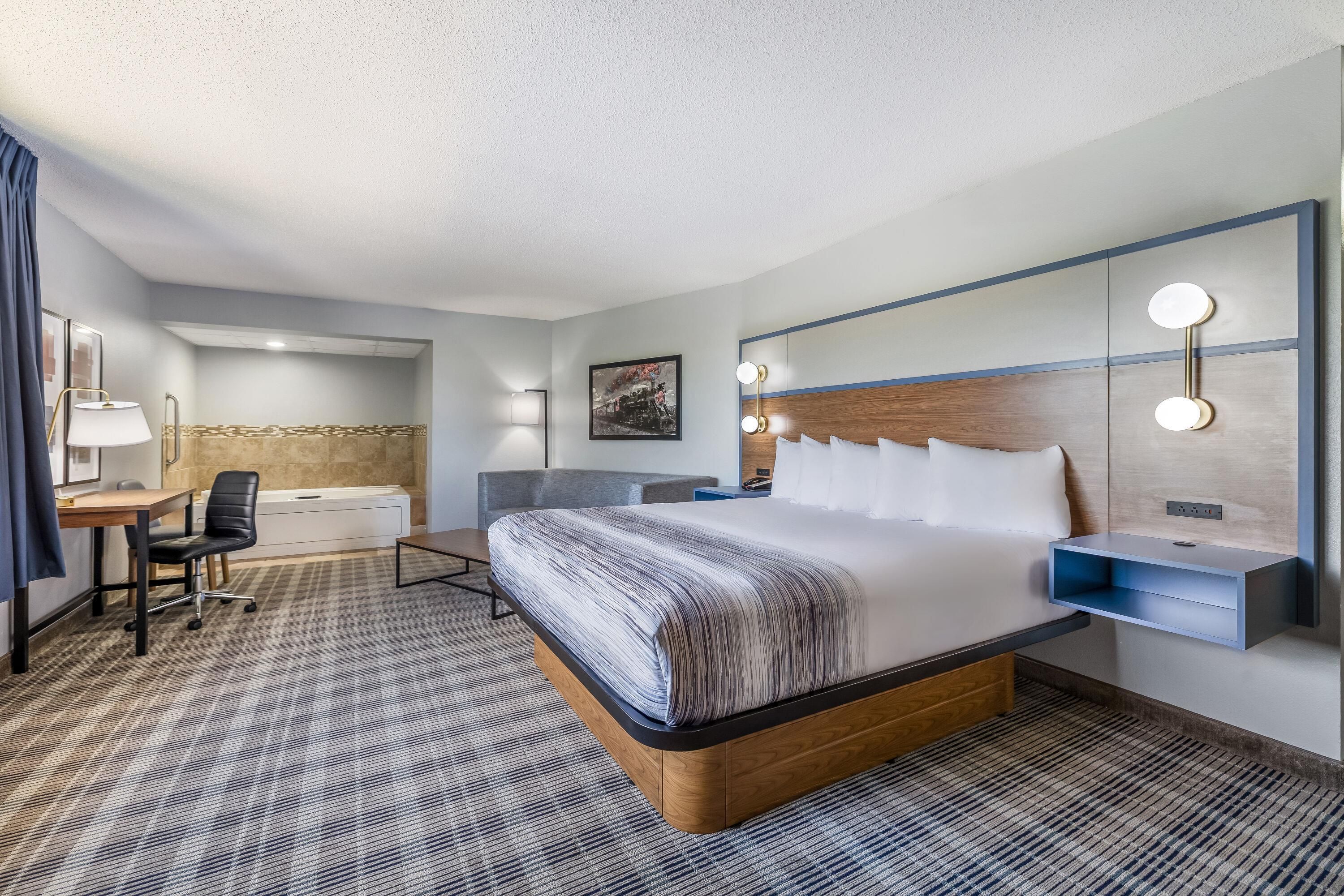 A hotel room with a large bed, a desk, a chair, a small table, and a bathroom.