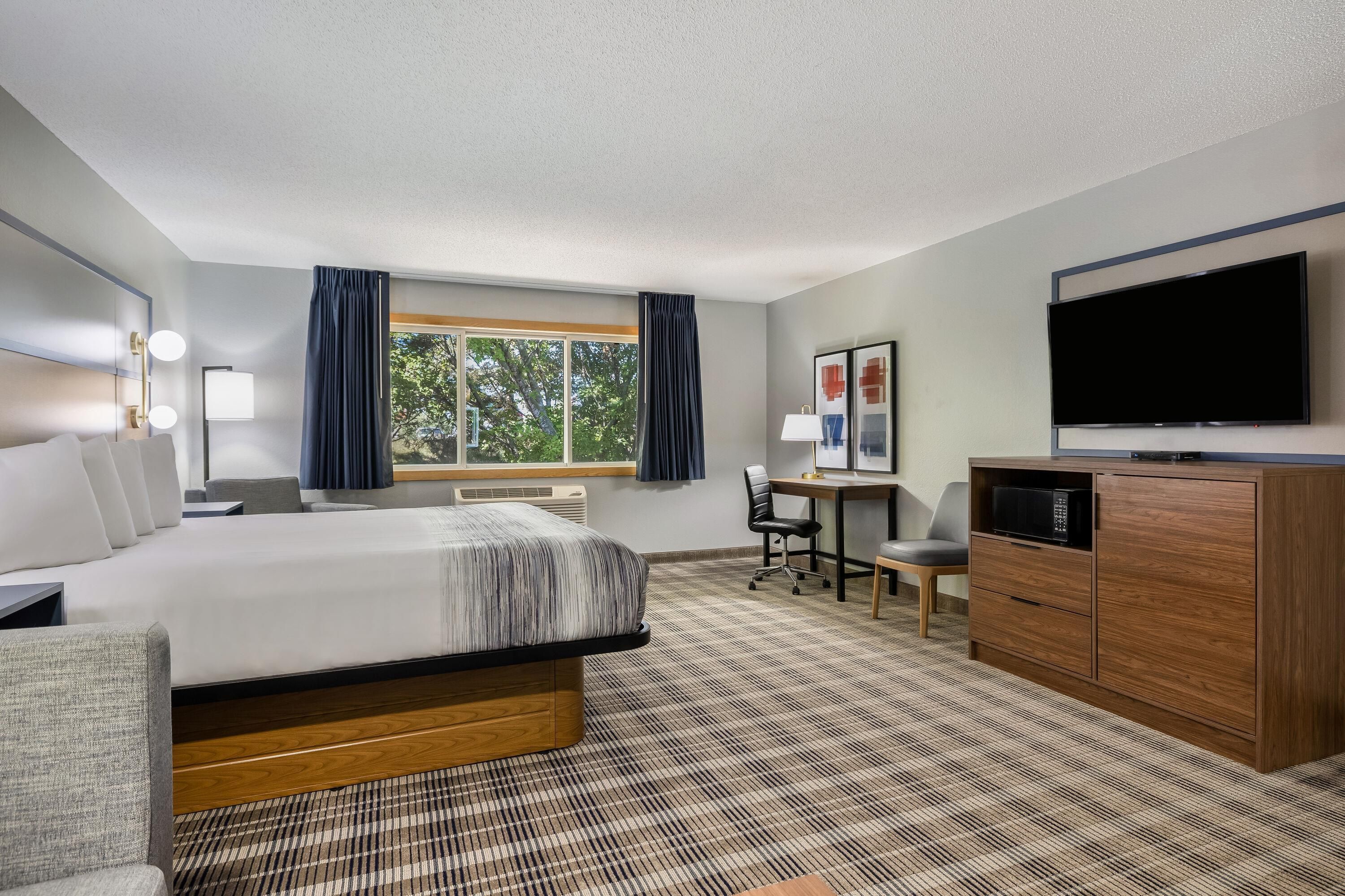 Ein Hotelzimmer mit Bett, Schreibtisch, Stuhl, Fernseher und Kleiderschrank.