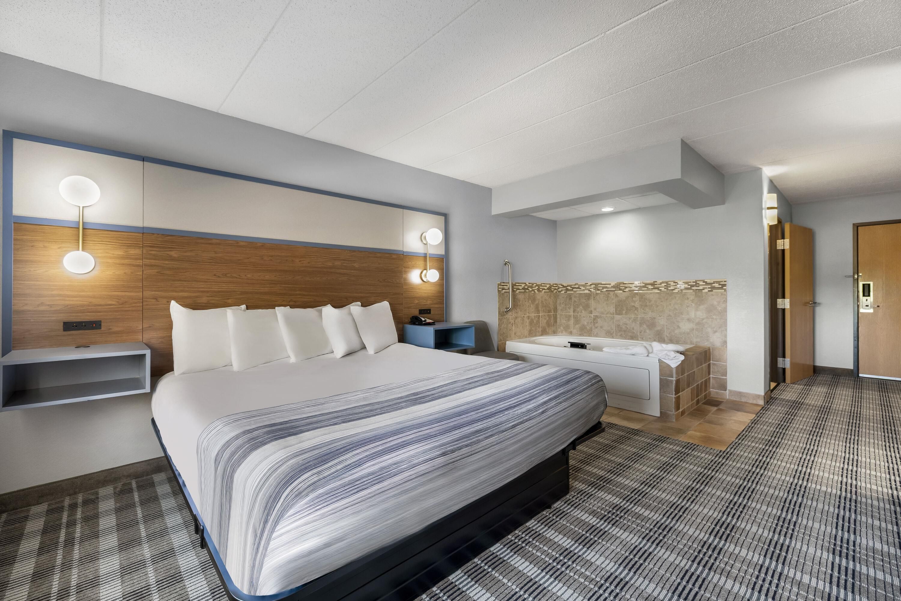 Una habitación de hotel con una cama grande, mesitas de noche, un tocador con espejo y zona de ducha.