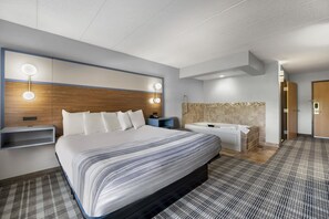 A hotel room with a large bed, bedside tables, a vanity with a mirror, and a shower area. - AmericInn by Wyndham Stillwater (Stillwater)