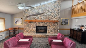 A cozy lounge area with a stone fireplace, plush seating, and a ceiling fan. - AmericInn by Wyndham Stillwater (Stillwater)