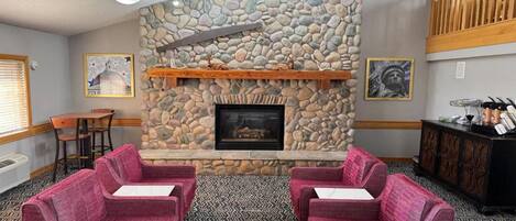 A cozy lounge area with a stone fireplace, plush seating, and a ceiling fan.