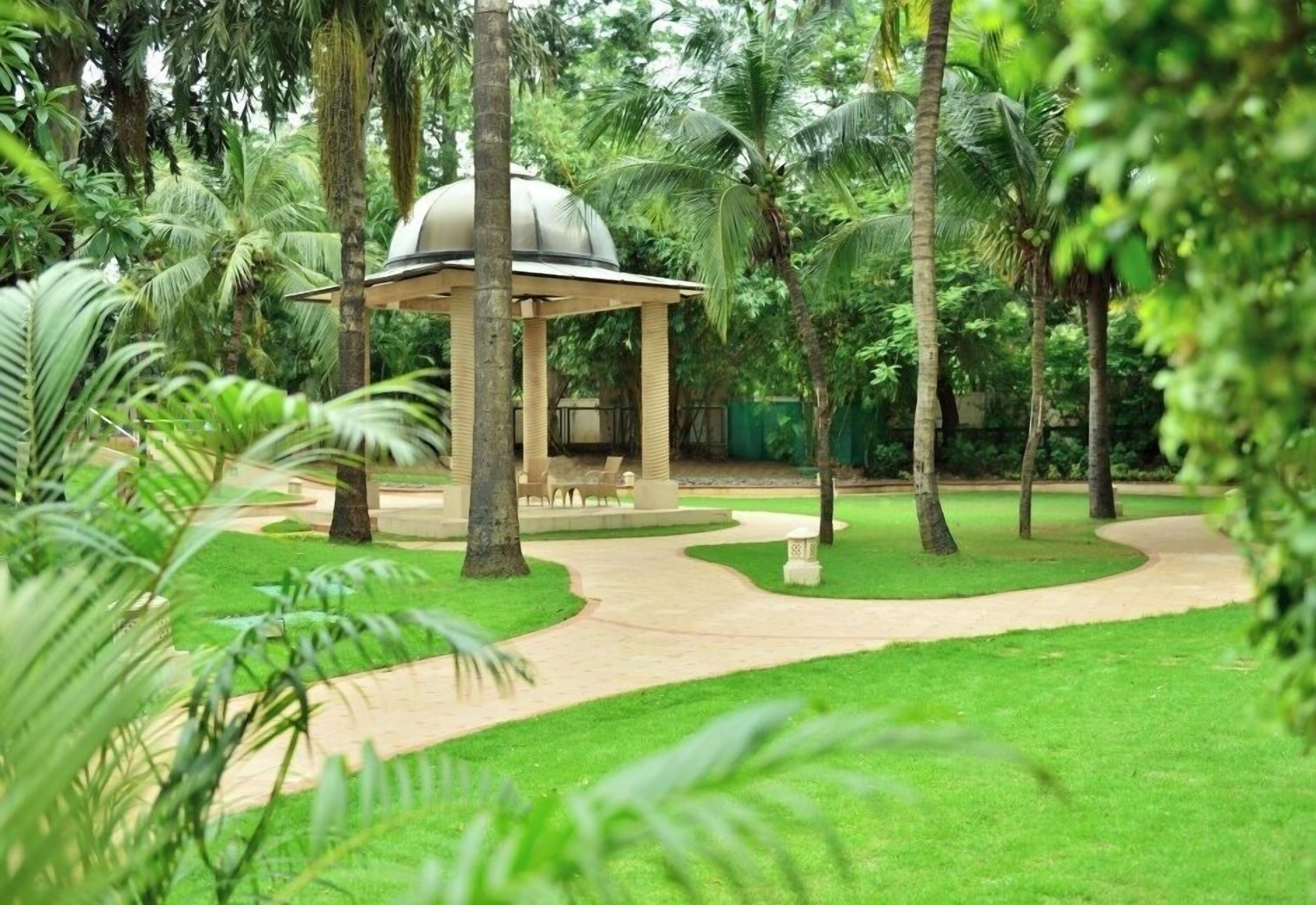 A gazebo with a dome roof surrounded by lush greenery and palm trees.