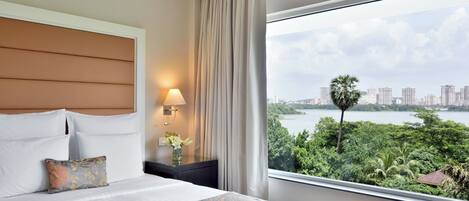 Una habitación de hotel con una cama grande, una mesita de noche con lámpara y una ventana con vista a la ciudad y al agua.