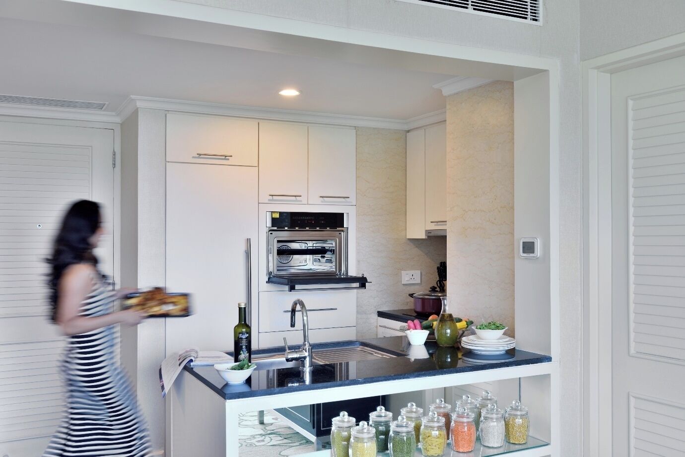 A compact kitchen with white cabinetry, a built-in oven, a sink, and a countertop with jars of spices.