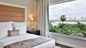Quarto de hotel com uma cama grande, uma mesa de cabeceira com abajur e vista para a cidade e para a água.