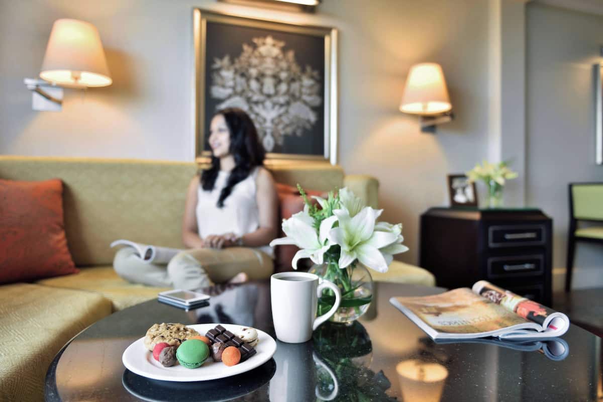 A room with a sofa, a coffee table with a plate of cookies and a mug, a magazine, and a vase with flowers.