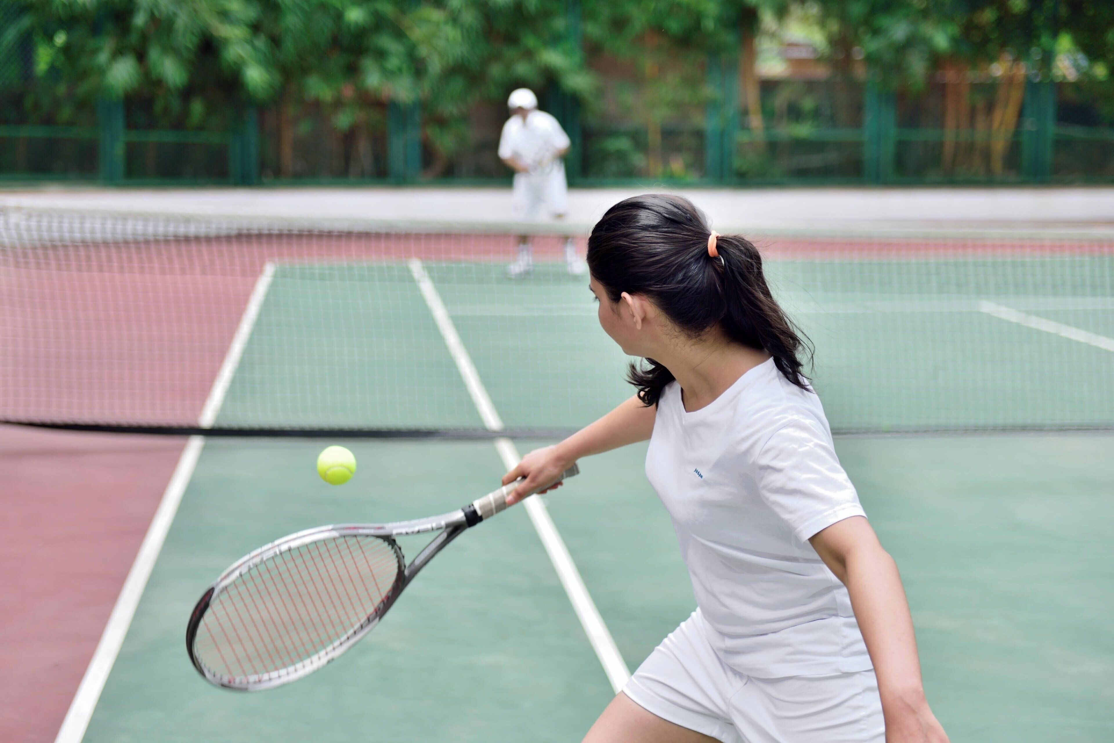 Un court de tennis avec un filet au milieu, un joueur vêtu de blanc et un autre joueur en arrière-plan.