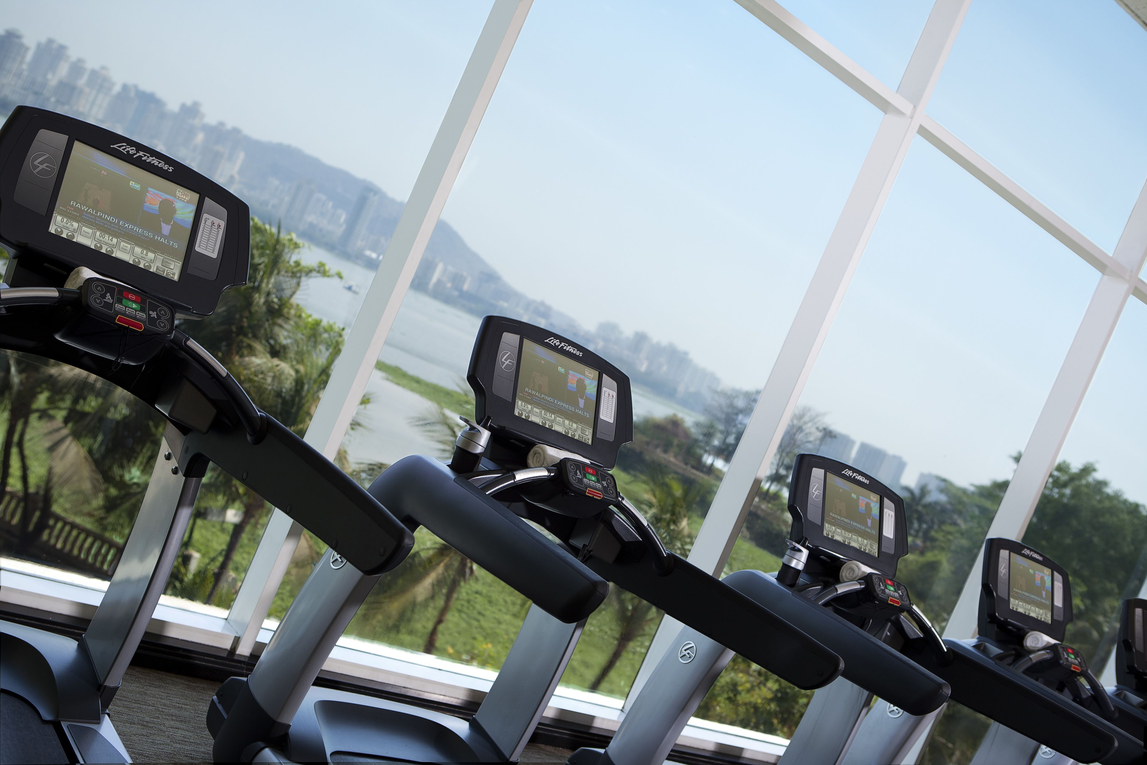 Three exercise bikes with digital displays, positioned in a room with large windows overlooking a body of water and greenery.