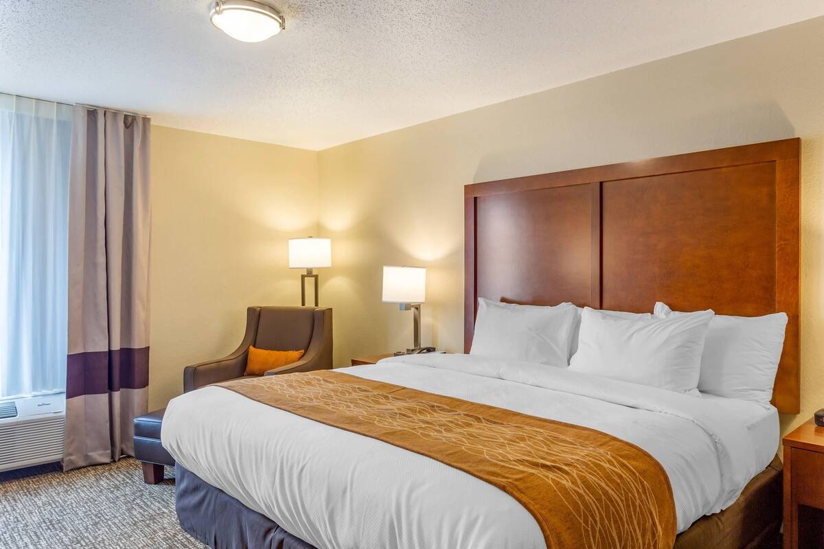 A hotel room with a large bed, two bedside lamps, a chair, and a window with curtains.