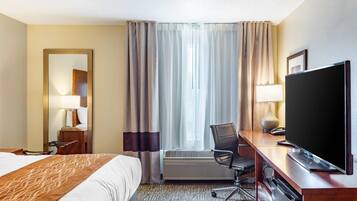 A hotel room with a bed, desk, chair, television, and a large window with curtains.