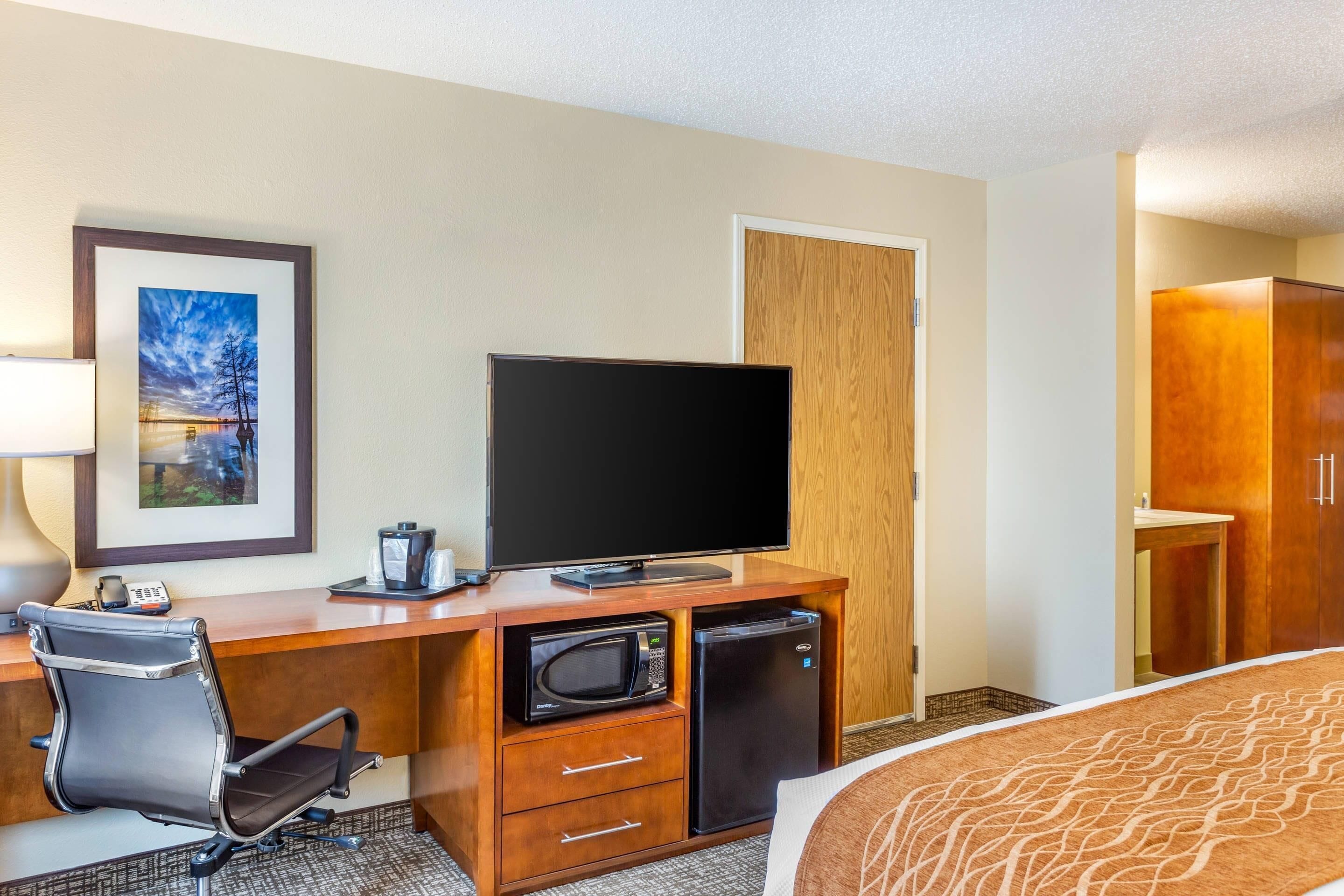 A hotel room with a desk, television, microwave, refrigerator, and a bed.