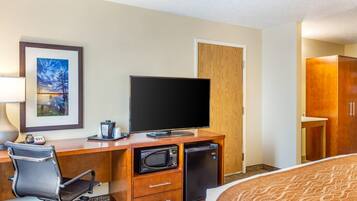 A hotel room with a desk, television, microwave, refrigerator, and a bed.