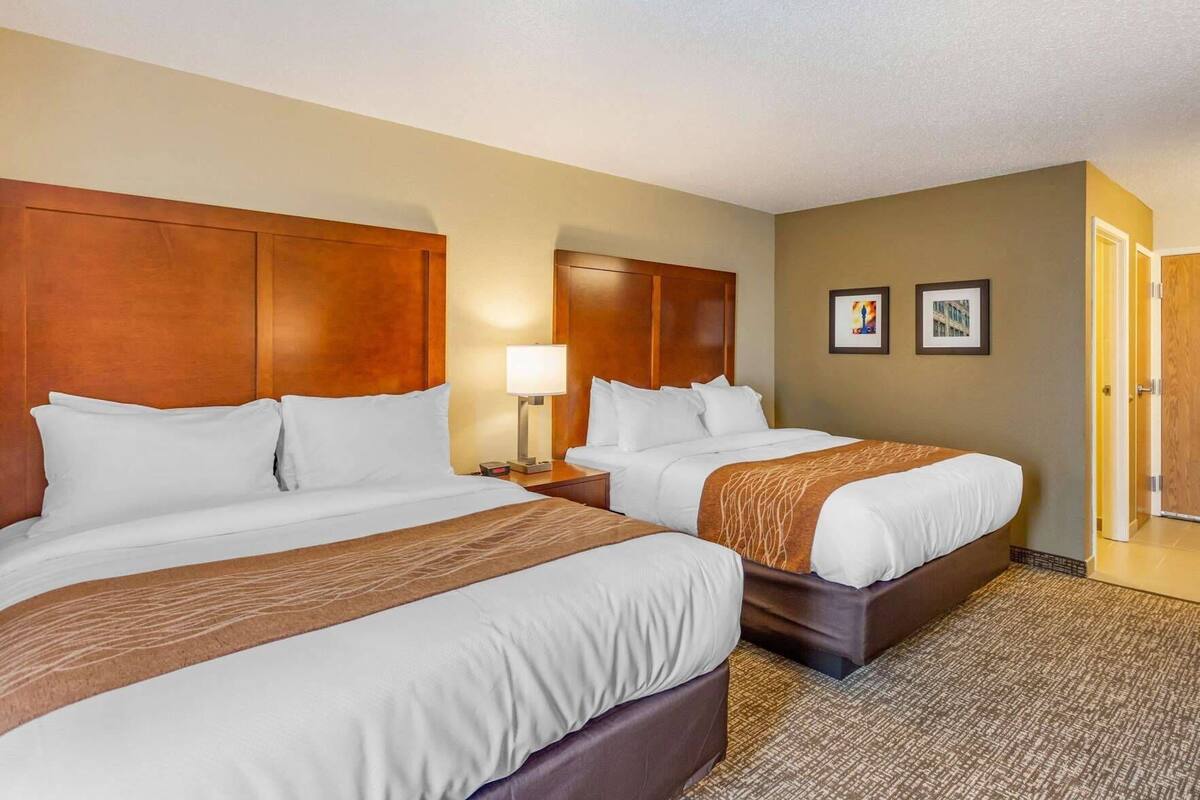 A hotel room with two beds, a nightstand with a lamp, a door, and a framed picture on the wall.