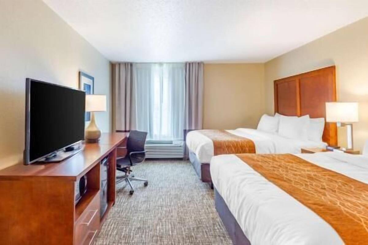 A hotel room with a TV, two beds, a desk, and a chair.