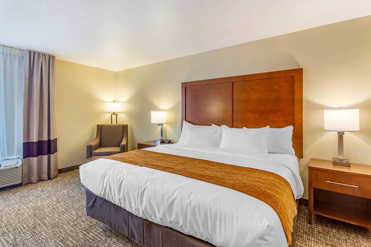 A hotel room with a large bed, two bedside tables with lamps, a chair, and a window with curtains.