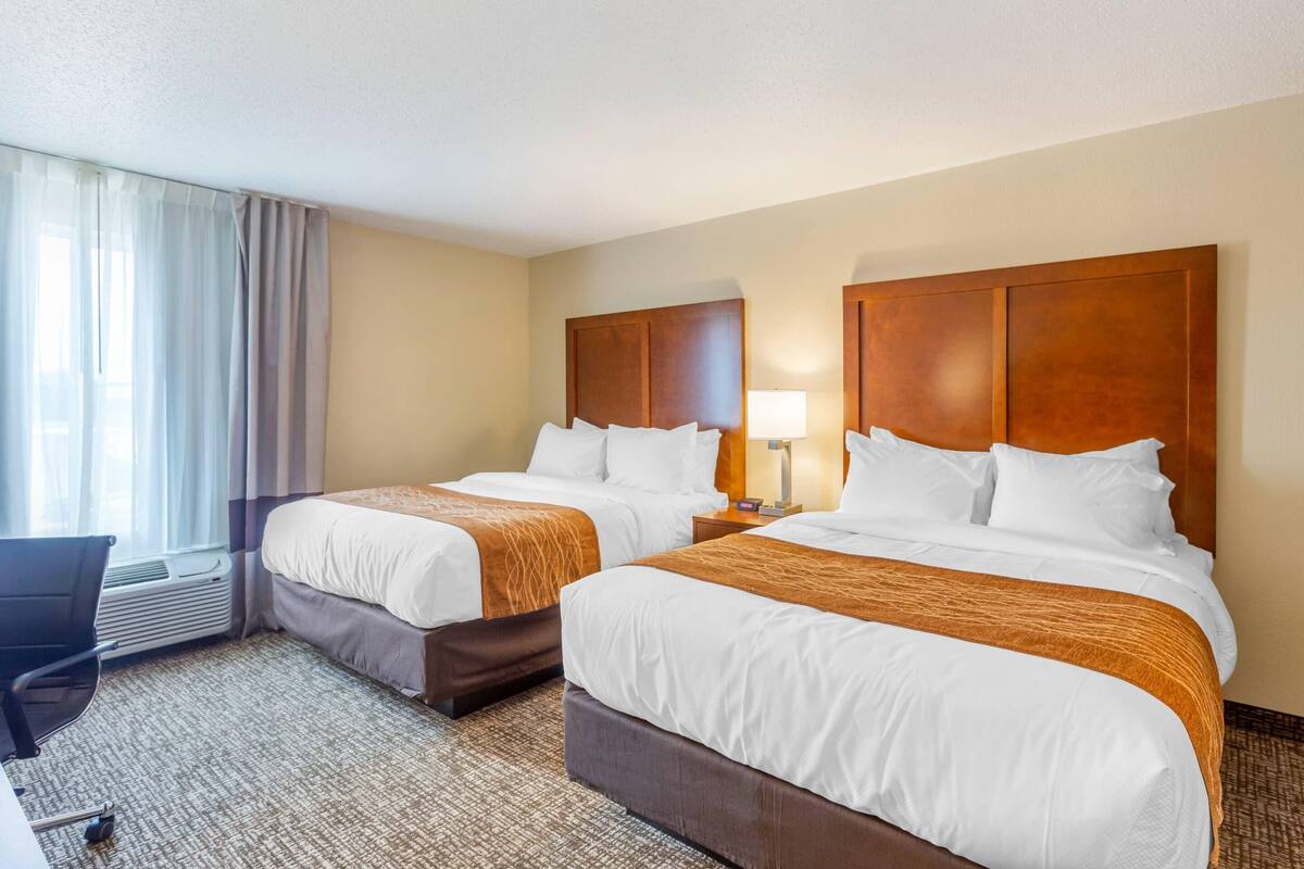 A hotel room with two beds, a desk, a chair, and a window with curtains.
