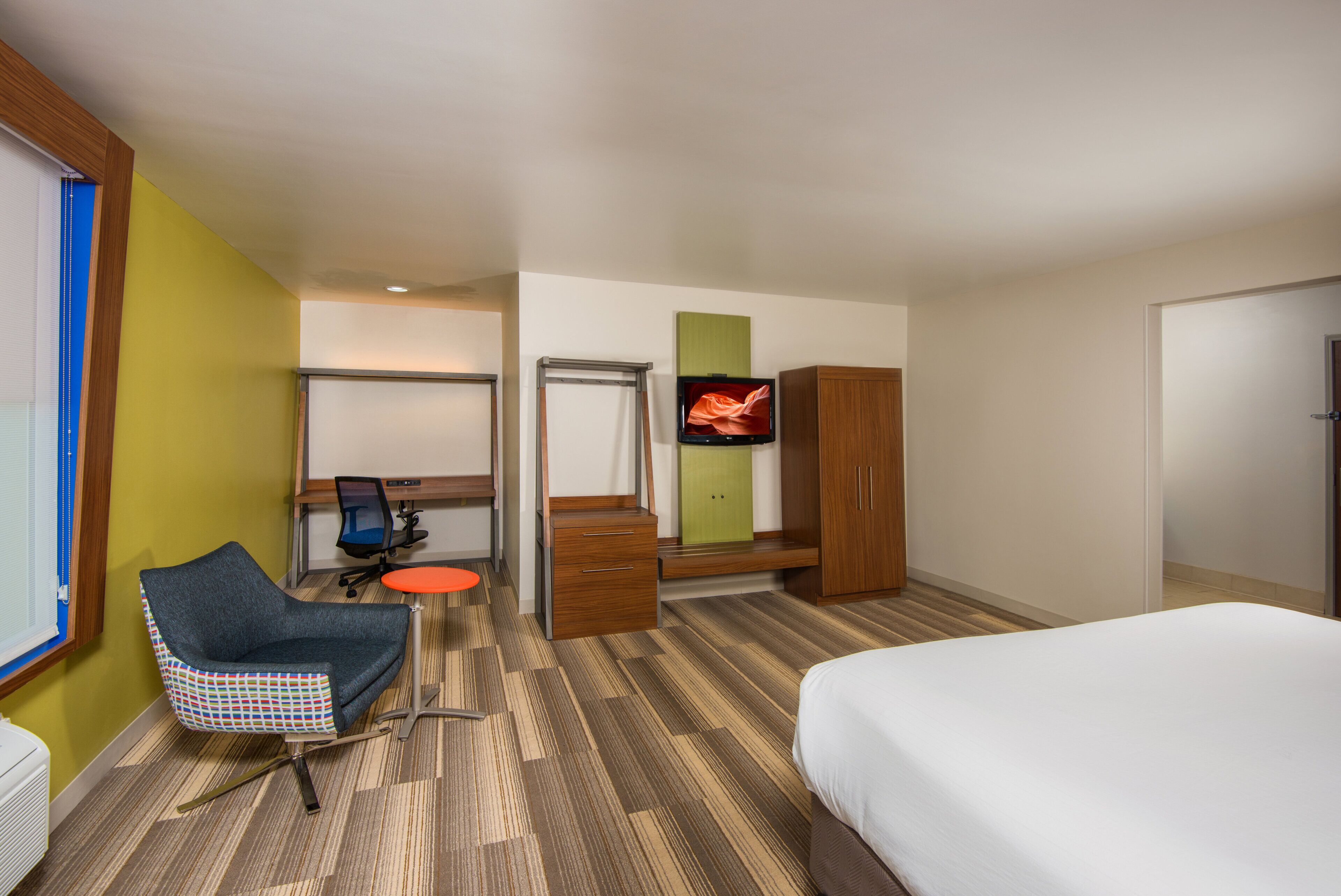 A hotel room with a bed, a desk with a chair, a television, and a wardrobe.