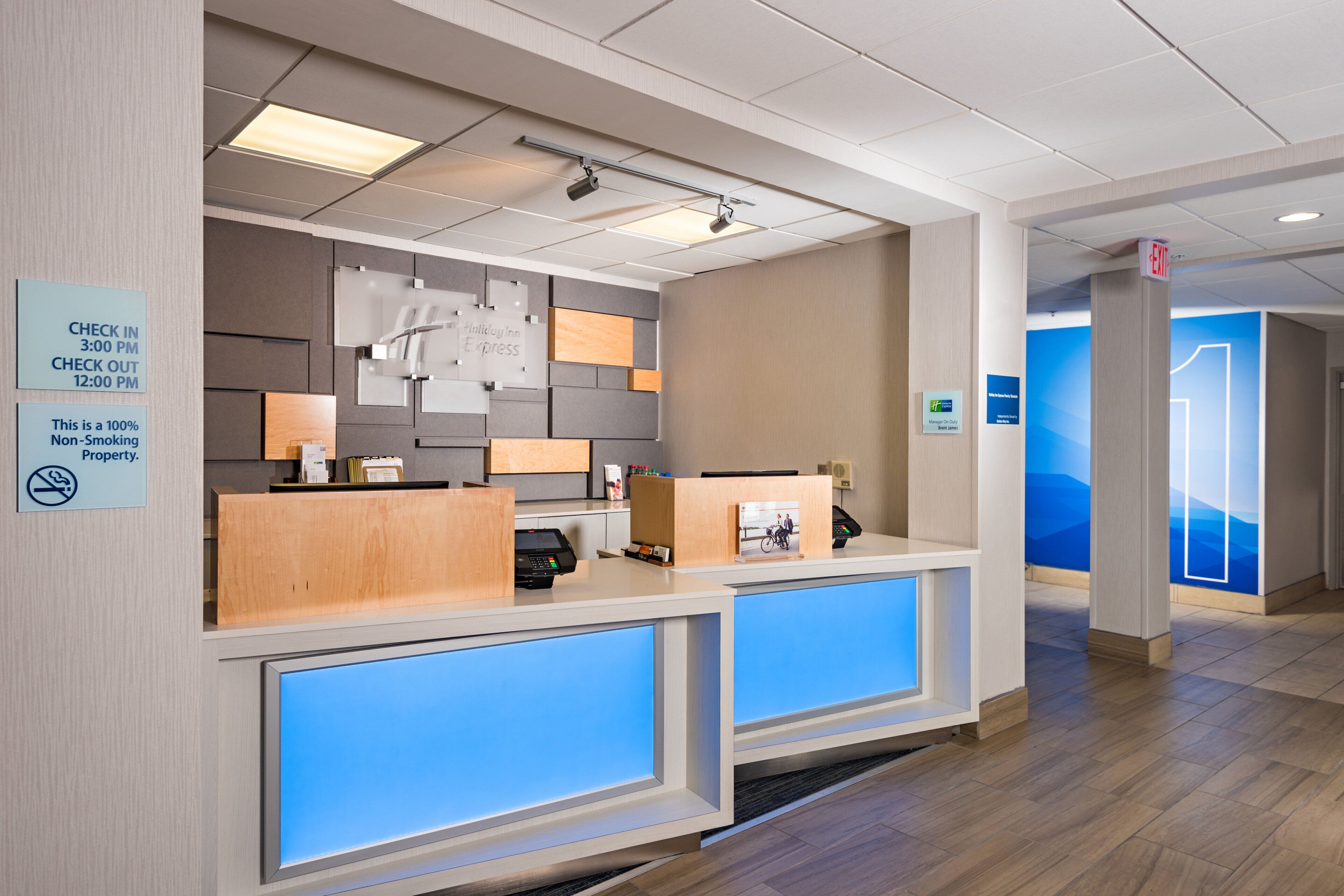En hotellreception med en skylt för in- och utcheckning, en skylt som anger att hotellet är rökfritt, och en digital skärm.