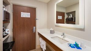 A hotel bathroom with a wooden door, a white sink, a mirror, and toiletries on the counter. - Holiday Inn Express Hotel & Suites PEORIA NORTH - GLENDALE by IHG (Peoria)