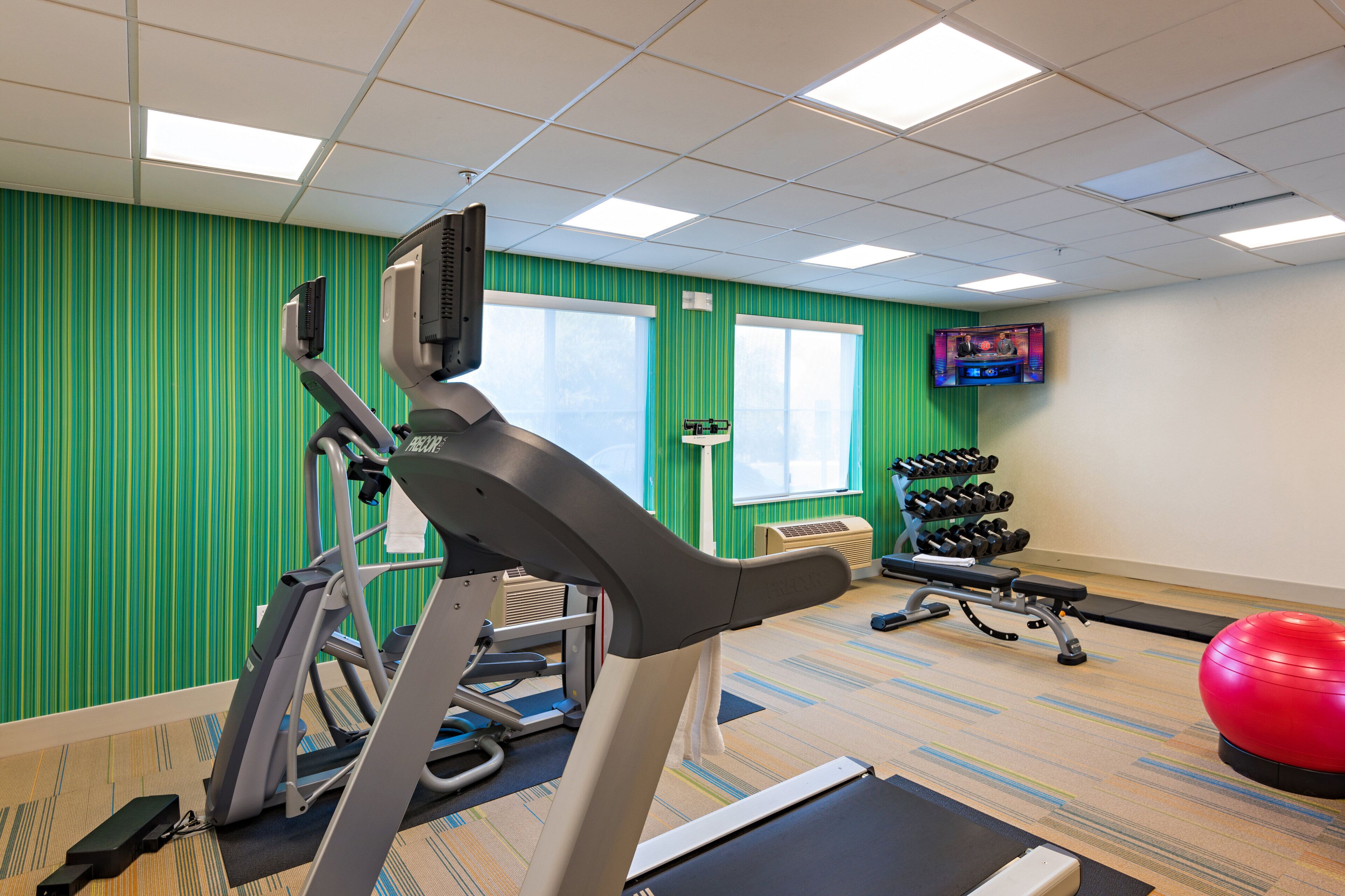 Un gimnasio con equipo de ejercicio, televisión y una pared verde a rayas.
