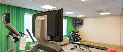 Un gimnasio con equipo de ejercicio, una televisión y una pared verde.