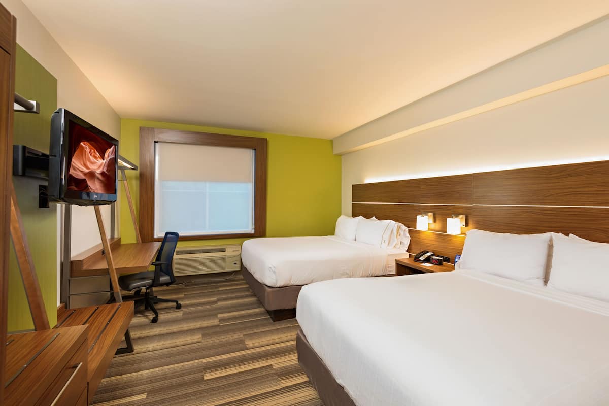 Ein Hotelzimmer mit zwei Betten, einem Schreibtisch, einem Sessel, einem Fernseher und einem Fenster mit Jalousien.