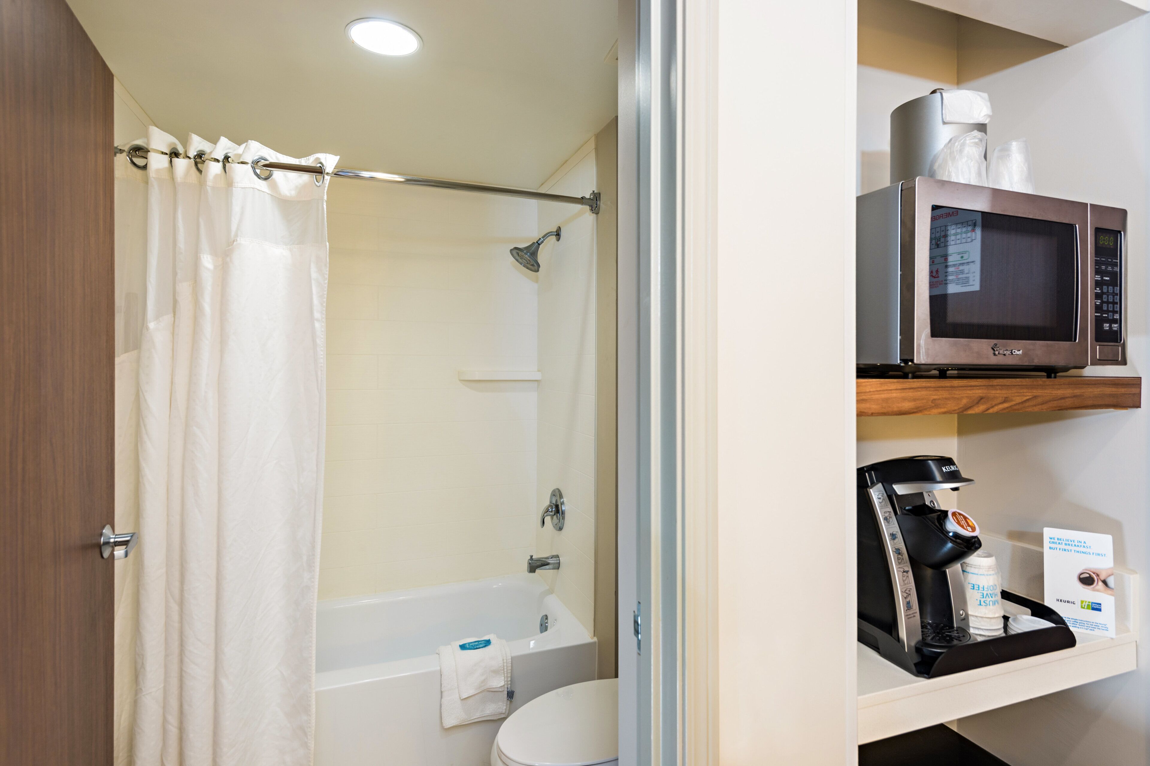 Un baño con cortina de ducha, bañera, inodoro, microondas y cafetera.
