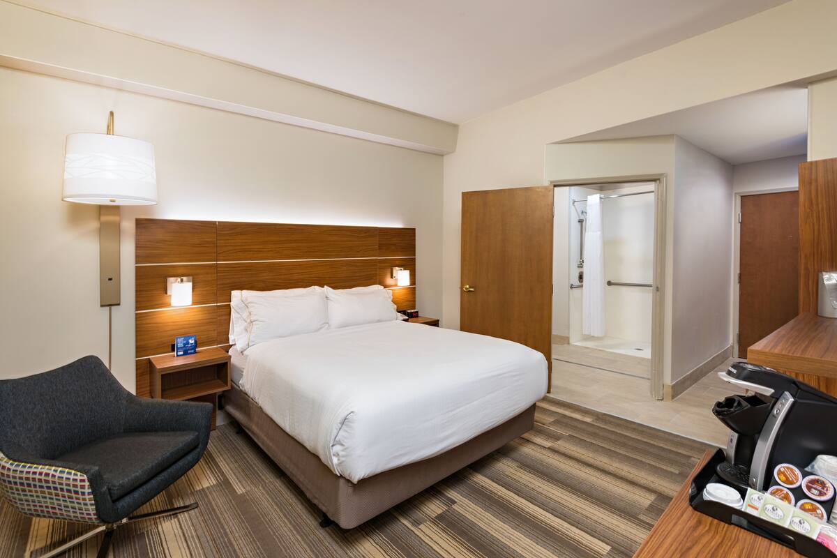 Ein Hotelzimmer mit einem großen Bett, einem Sessel, einem Schreibtisch mit Kaffeemaschine und einem Spiegel.