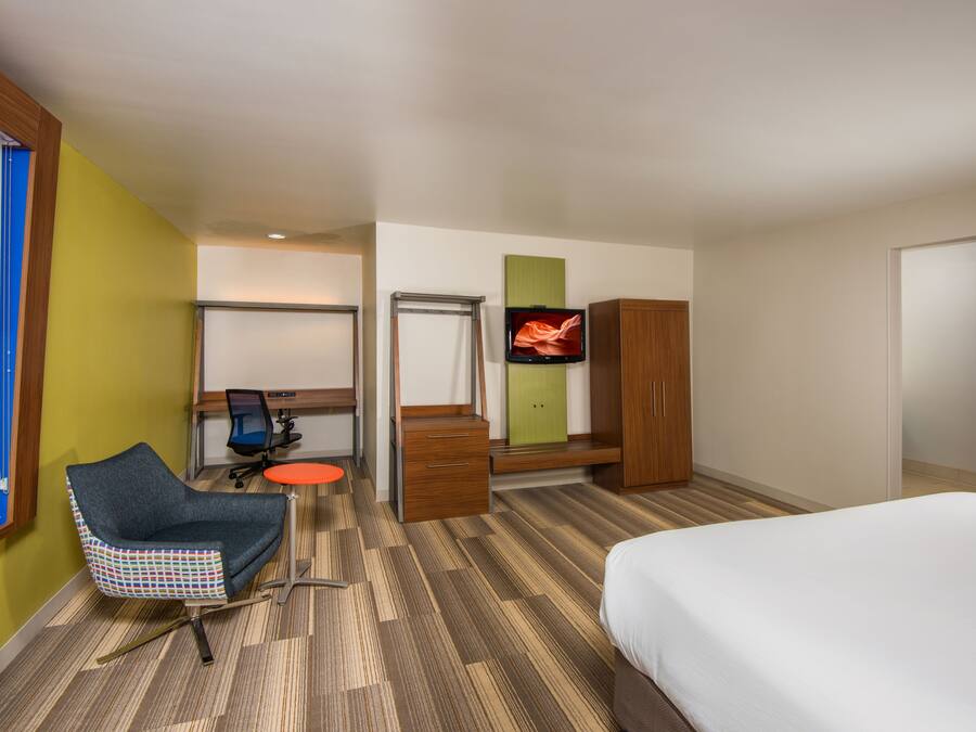 Una habitación de hotel con cama, escritorio, silla, televisor y armario.