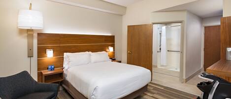 A hotel room with a bed, bedside tables, a chair, a desk with a coffee machine, and a bathroom with a shower and toilet.
