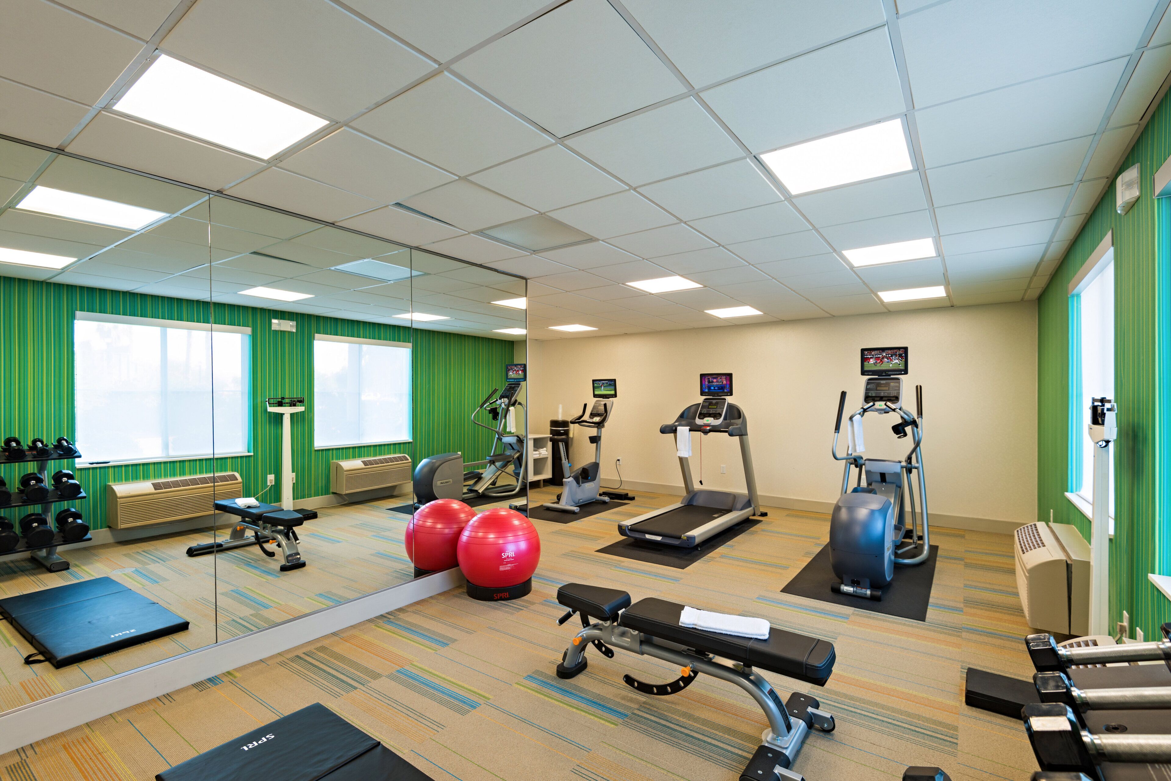 Une salle de sport équipée de divers appareils d’exercice, notamment des tapis de course, des vélos d’appartement et des poids libres.