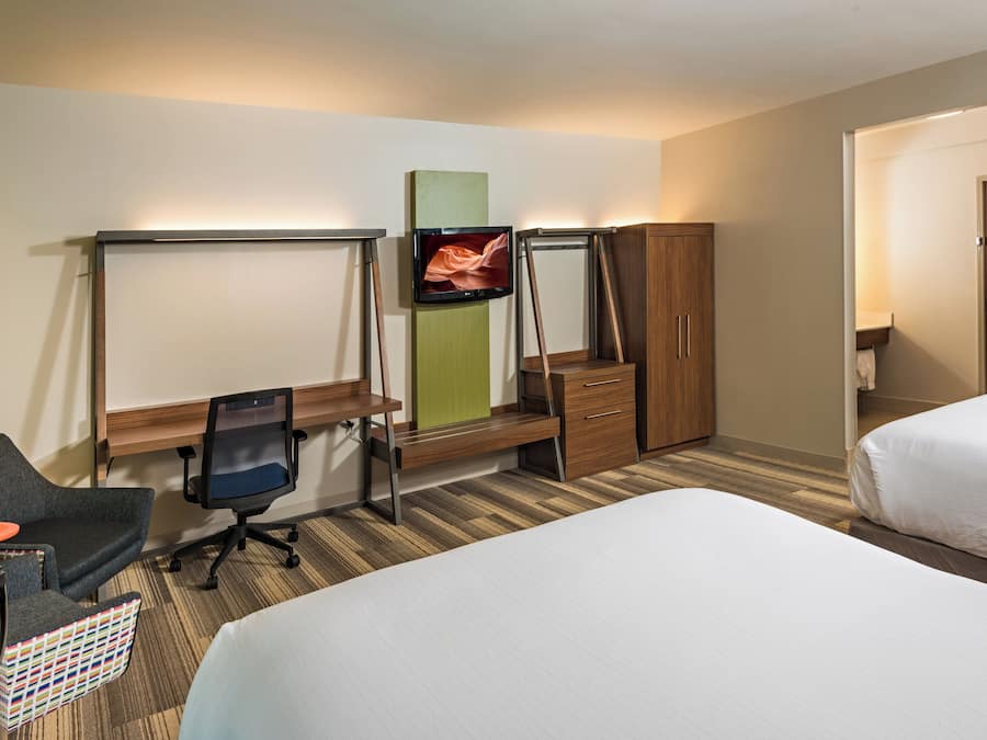 Una habitación de hotel con una cama, un escritorio con una silla, un televisor y un armario.