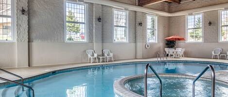 Una piscina interior con agua cristalina, rodeada de sillas blancas y una pequeña mesa.