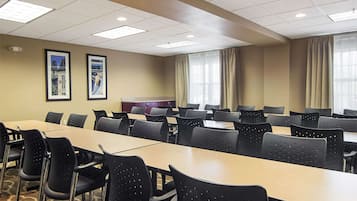 Un salón de conferencias con varias mesas y sillas, cuadros en la pared y un ventanal con cortinas.
