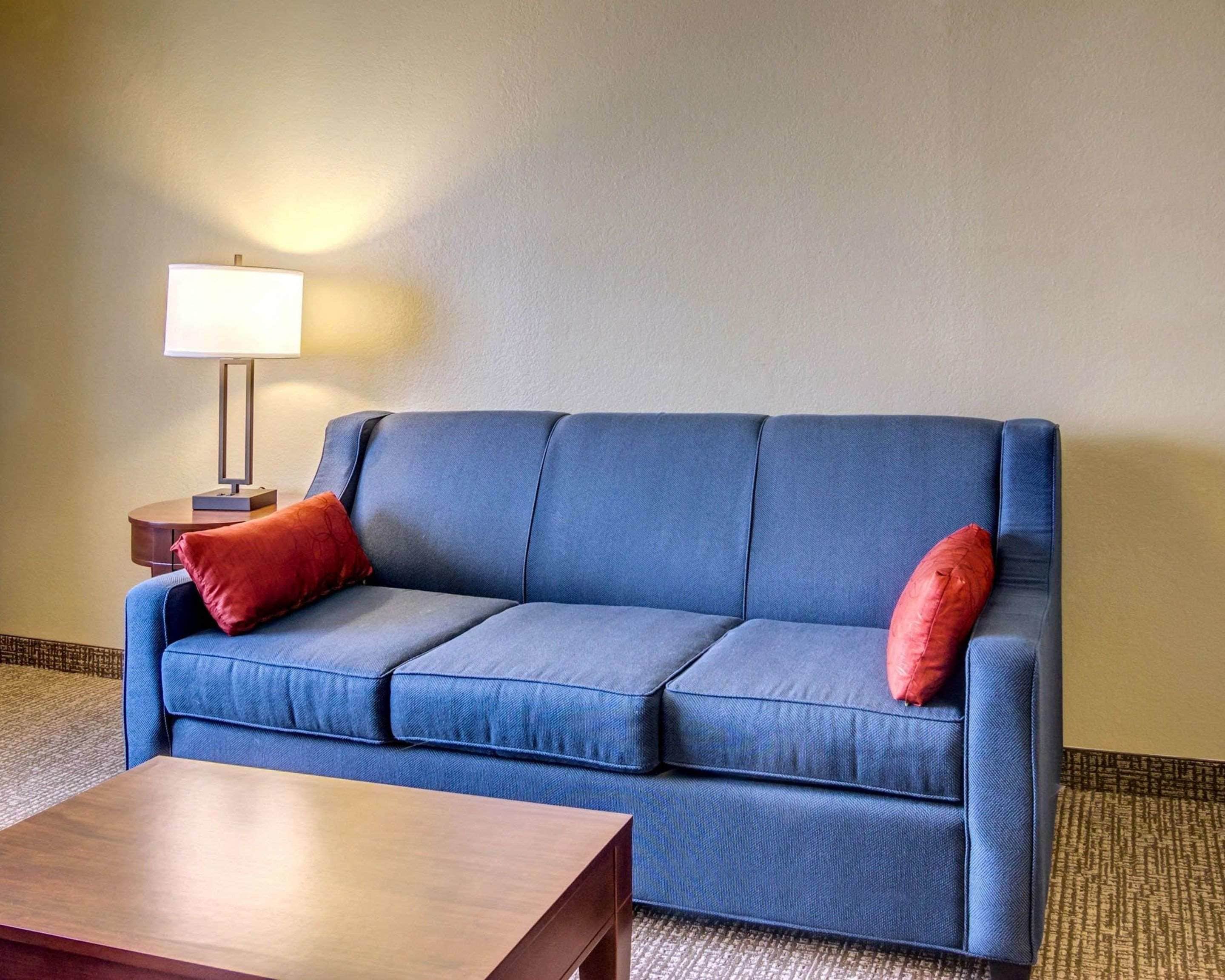 Un sofá azul con dos almohadas rojas, una mesa de centro de madera y una lámpara sobre una mesita auxiliar.
