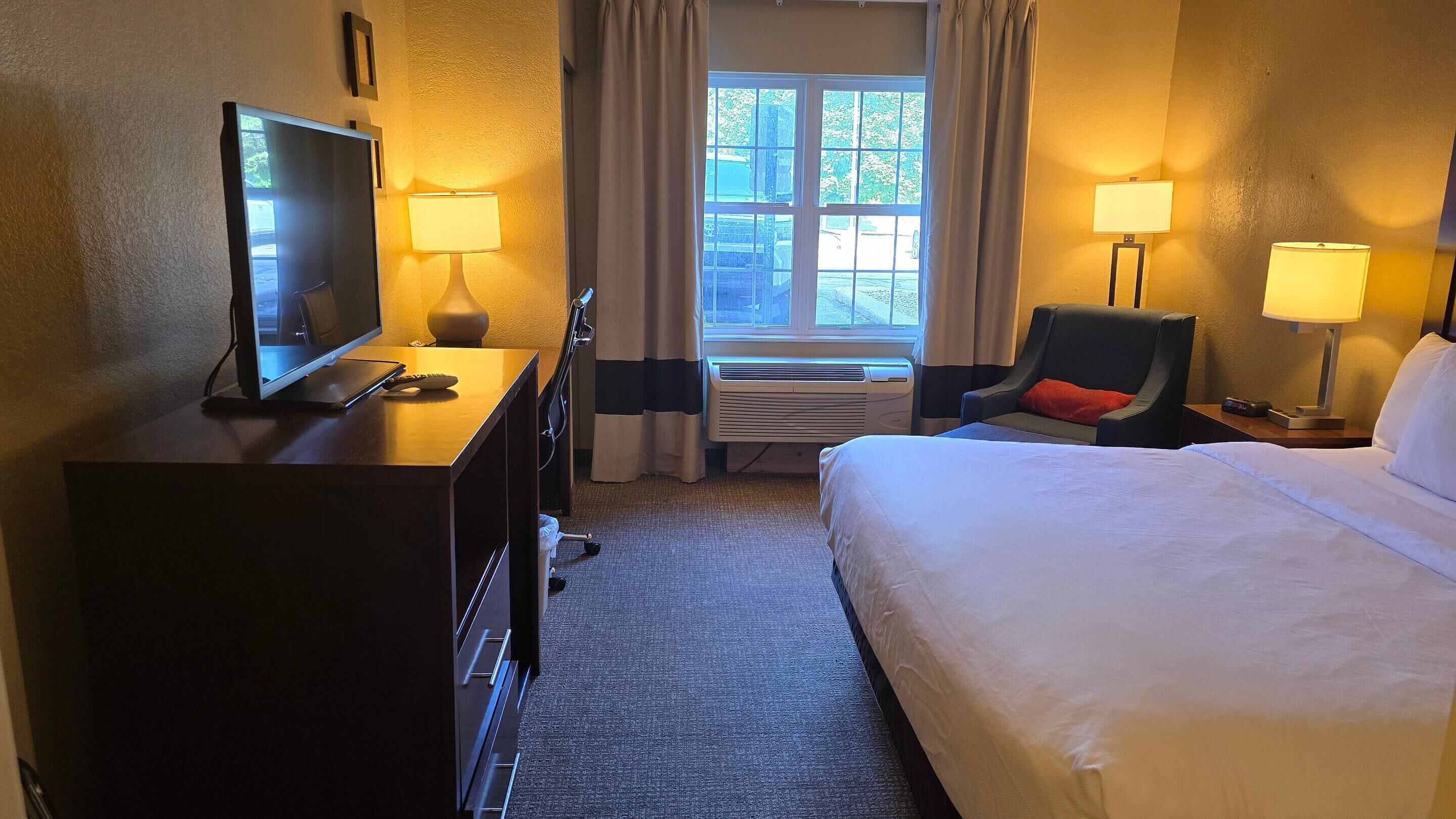 Une chambre d’hôtel comprenant un lit, un bureau avec une télévision, une chaise et deux lampes.