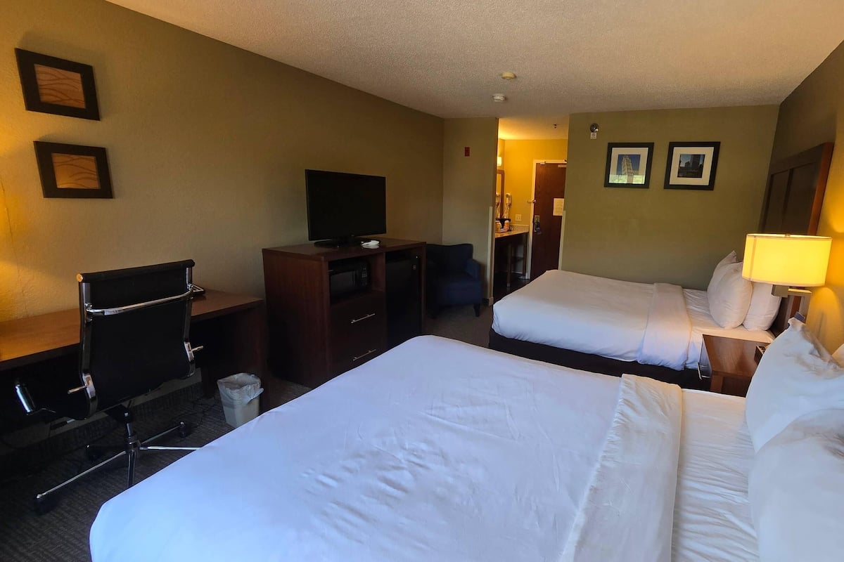 Une chambre d’hôtel avec deux lits, un bureau, une chaise, une télévision et une lampe.